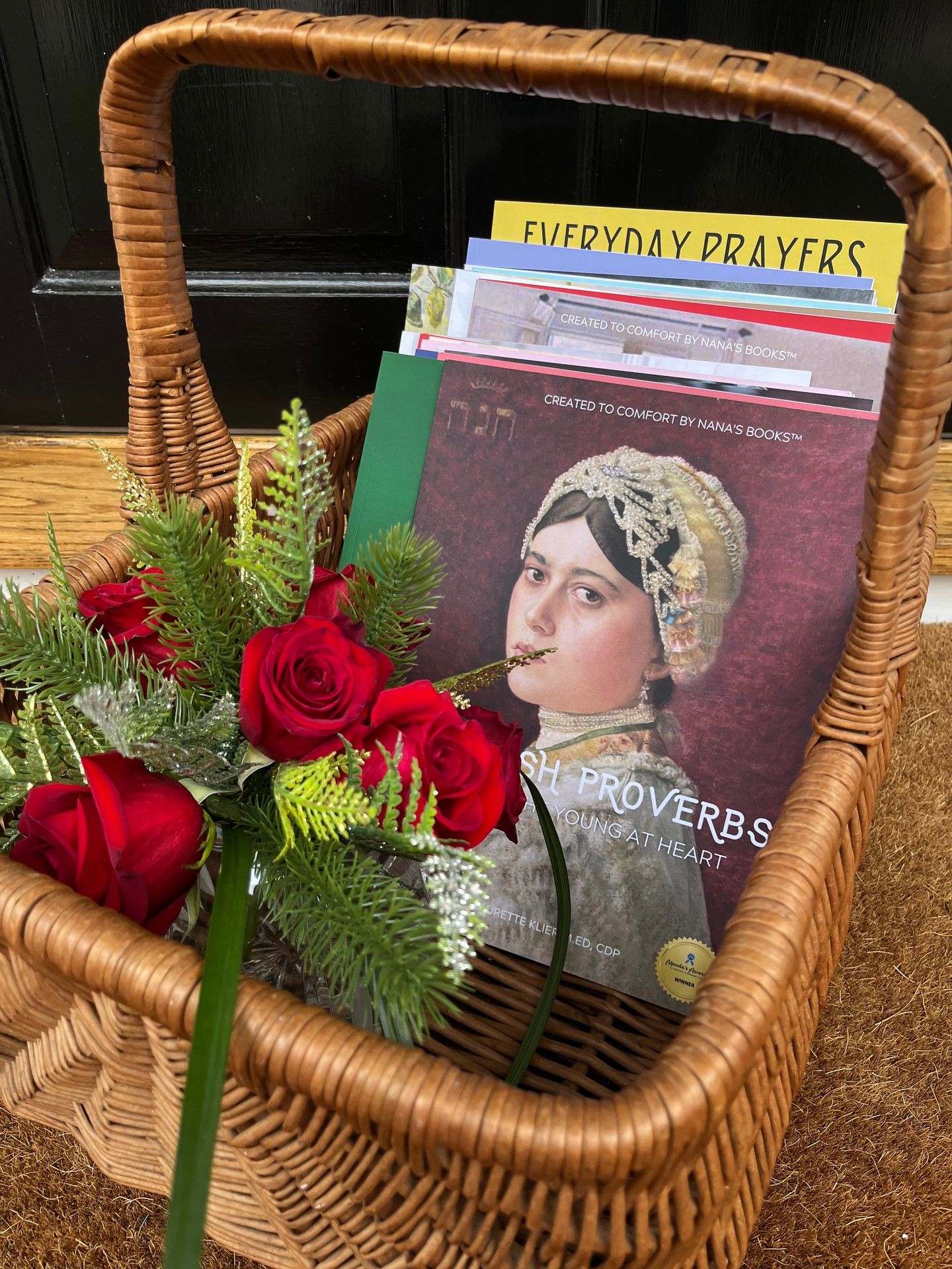 This is a basket of NANA’S BOOKS, designed for people living with dementia. the first book in front is a book of Jewish Proverbs and there is a round cut crystal bowl full of red tea roses in the basket to bring on connected visits. NANA’S BOOKS are faith-based and many have a spiritual focus.