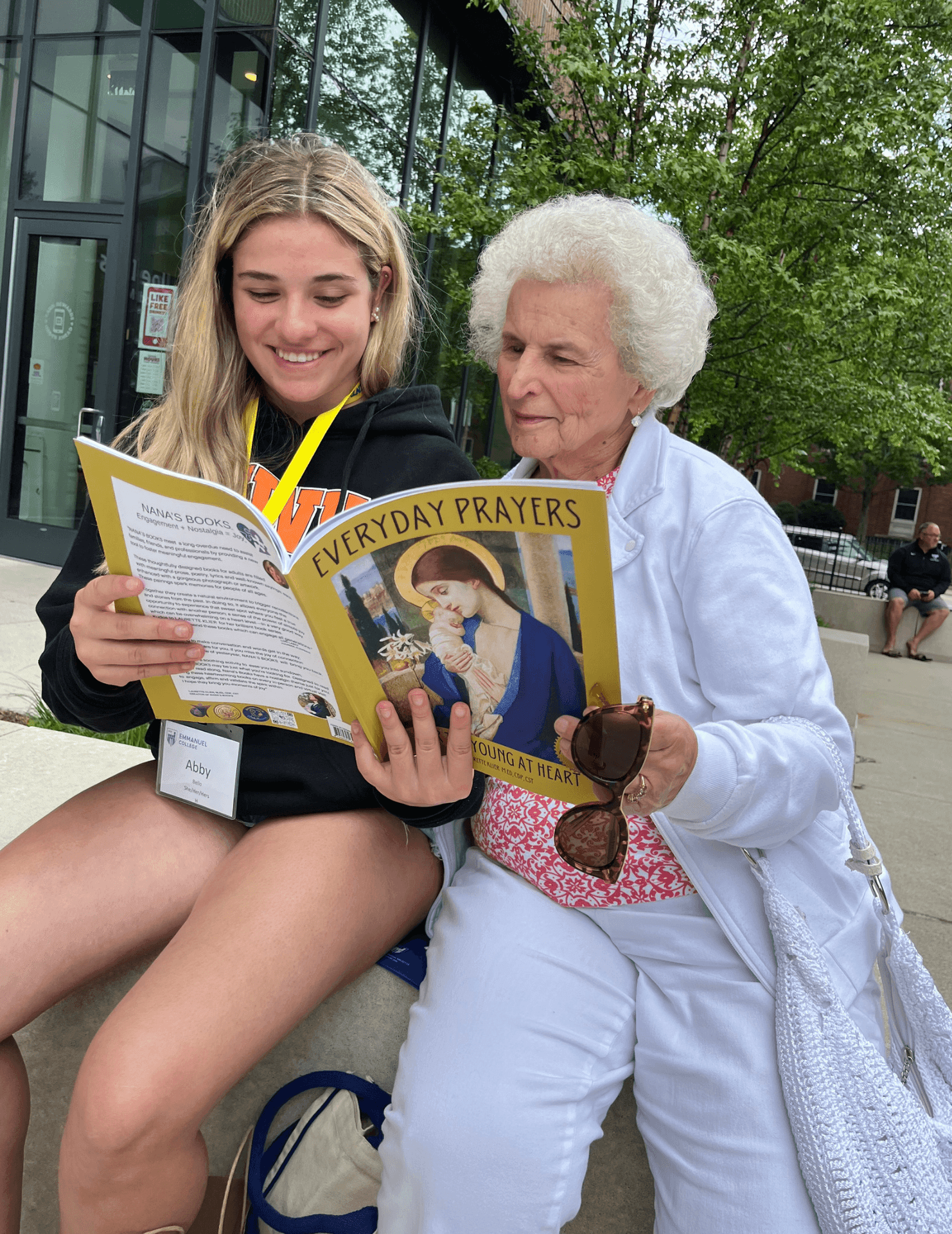 An older woman with dementia reading NANA’S BOOKS with her granddaughter on Emmanuel College’s campus. NANA’S BOOKS are for people living with dementia.