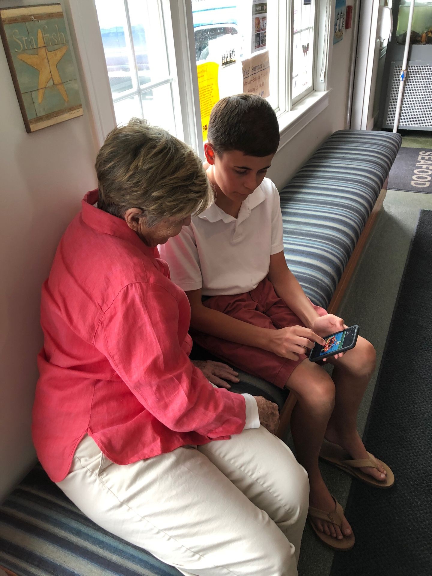 This is a picture of a young boy reading aloud to his grandmother from NANA’S BOOKS’ digital library. She is wearing a bright pink linen top and they are happily sharing a moment.  NANA’S BOOKS unite generations and help care partners and clinicians with engaged conversations through dignified reading and age and ability-appropriate books.